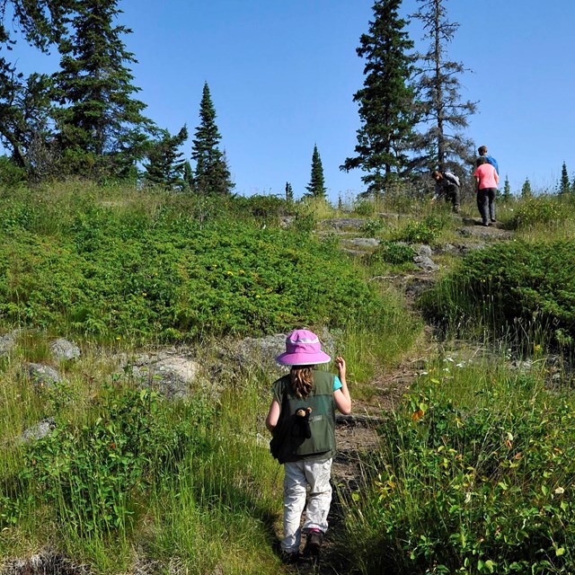 People hike up a rocky trail to a ridge top. 