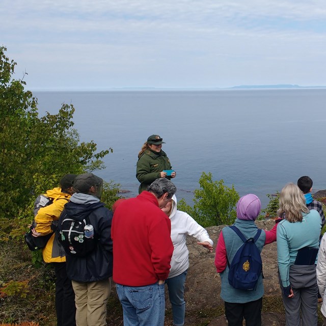 A park ranger speaks to a group of people as they look at Lake Superior and the Canadian shoreline.