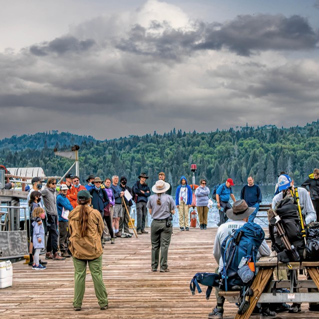 People gather around a park ranger on a dock.