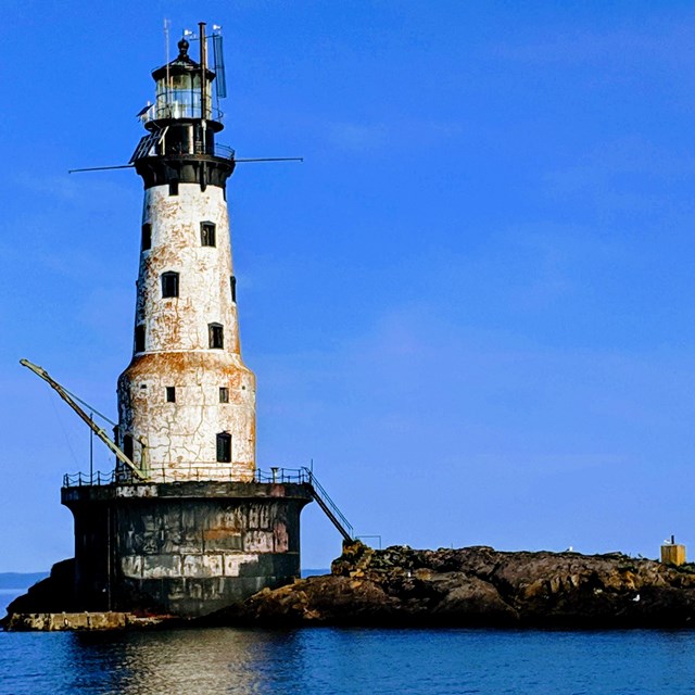 lighthouse standing on a rocky reef on a blue sky day