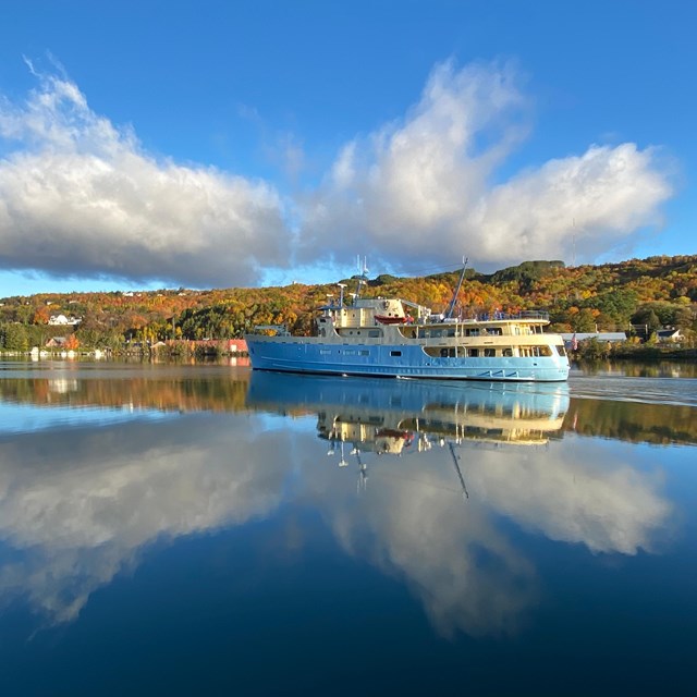 Ranger III traveling the Portage Wateway. Clouds in a blue sky reflect off the water.