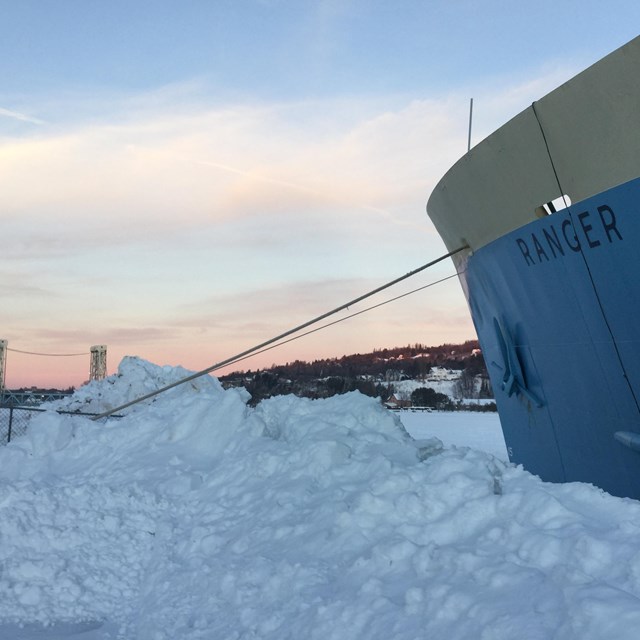 RANGER III bow in winter. Snow drifts crowd the frozen bow line. Houghton lift bridge in distance.
