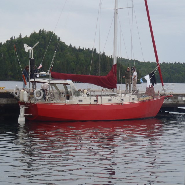 A red sailboat is tied to a dock with an island in the background and water.