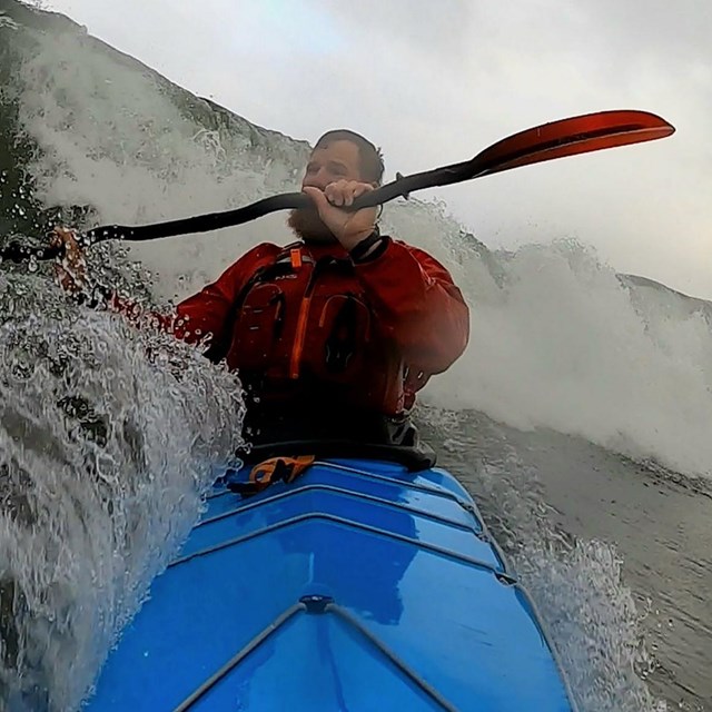 A man in a kayak paddles against strong wind and waves on Lake Superior on a stormy day.