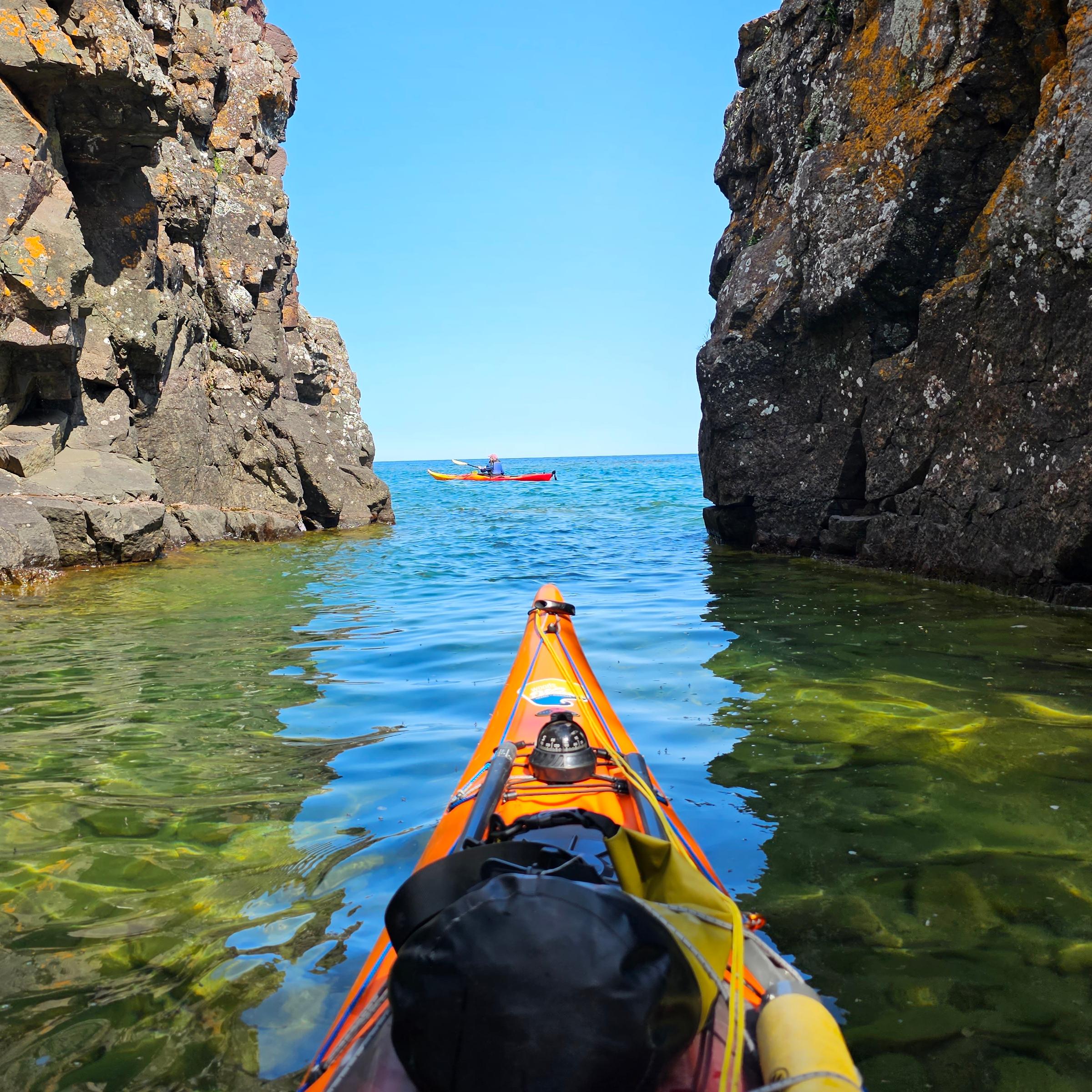 A yellow kayak maneuvers between two rocky cliffs on a calm sunny day in Lake Superior.