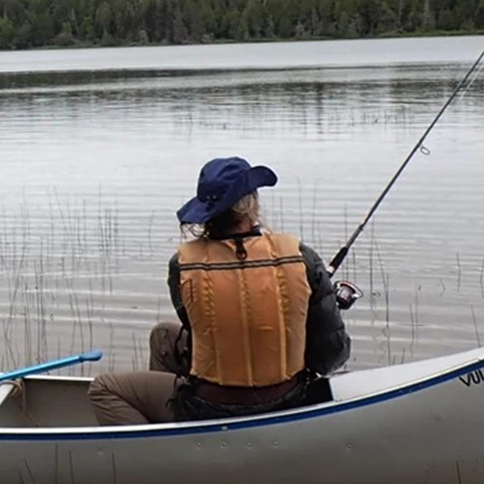 Two people sit in a canoe fishing on an interior lake.