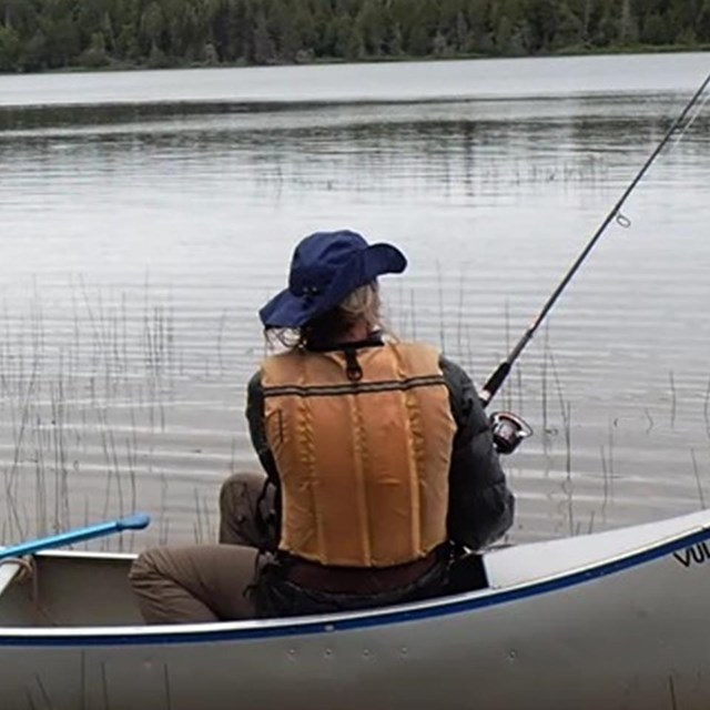 Two people sit in a canoe fishing on an interior lake.