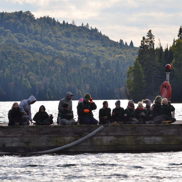 Several kids sit on a dock with a scenic lake in the background