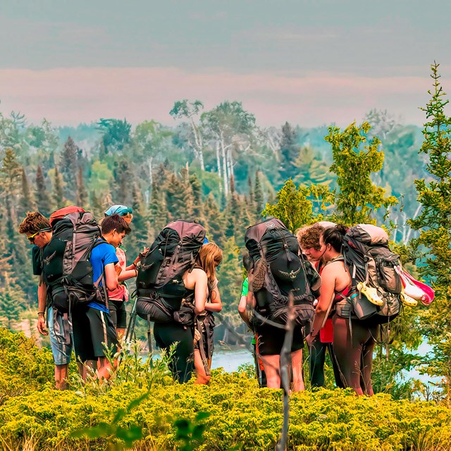 A group of nine people with large backpacks and gear stand in a circle.