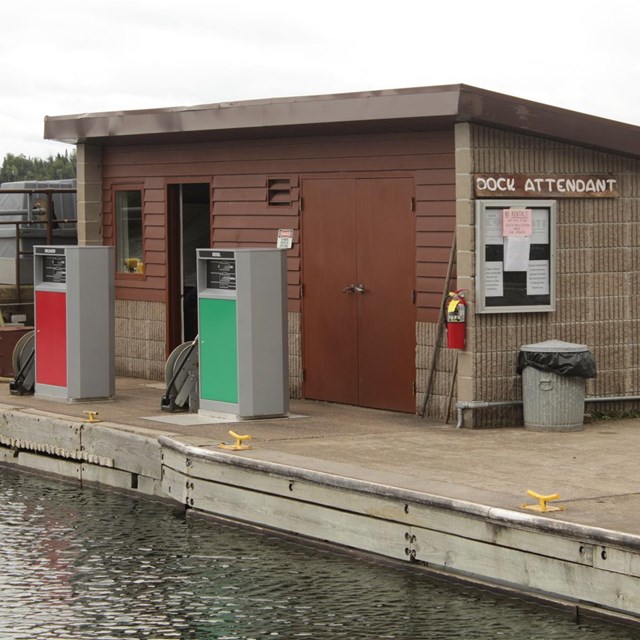 Two fuel pumps sit on a dock with a small building in the background