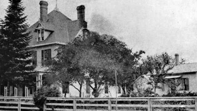 a white framed house surrounded by a whote fence in the front of the home