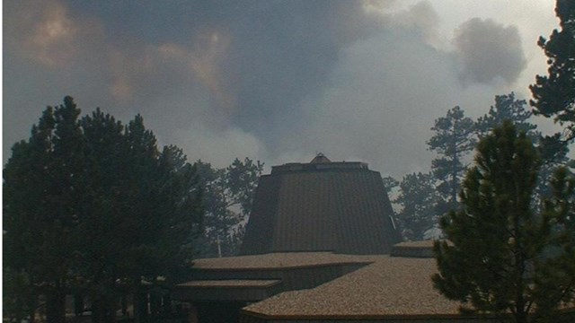Image of the Jewel Cave National Monument visitor center with billows of smoke behind it.