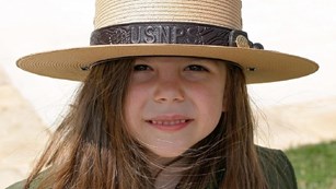 A young girl dressed as a Junior Ranger with a badge and ranger hat.