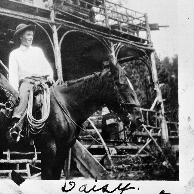 Photo of a man riding a horse in front of a wooden two-story lodge.