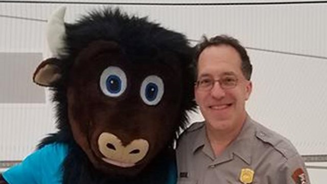 photo of uniformed ranger Richard Fefferman with a buffalo mascot who is wearing a blue shirt