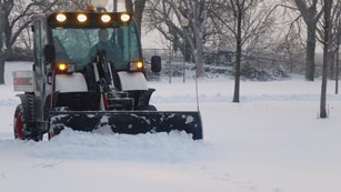 Color image of a green plow clearing snow off a walkway in the Gateway Arch National Park.