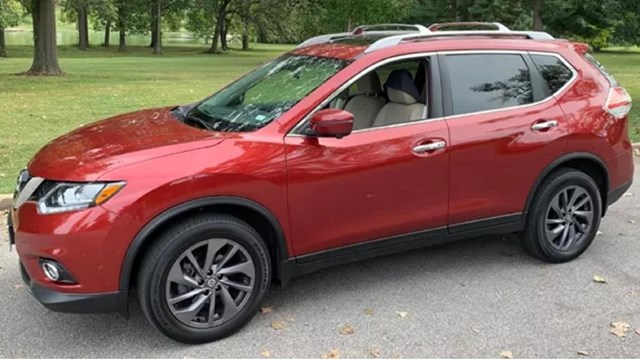 A red car (SUV) parked on pavement. Green grass and trees in the background. 