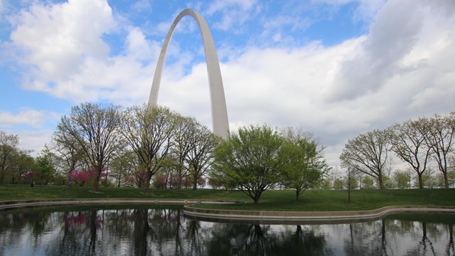 The Gateway Arch, with a pond and trees in the foreground and a bright blue sky in the background