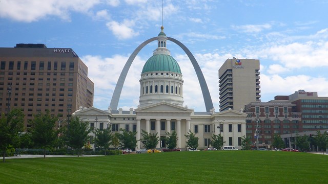 An ornate white building with a green top. The Gateway Arch is in the background.