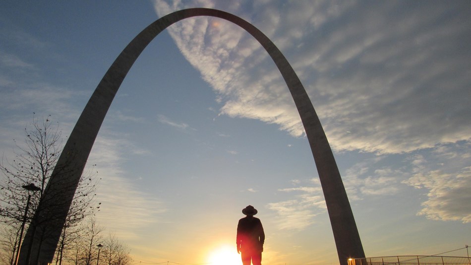 the silhouette of a ranger and the Gateway Arch at sunrise