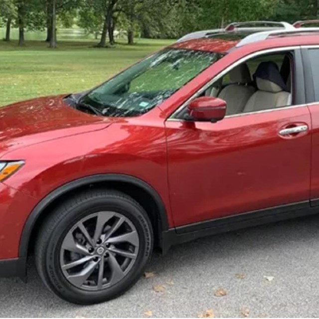 A red car (SUV) parked on pavement. Green grass and trees in the background. 