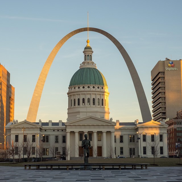 Image of 630 foot steel arch with green and white stone courthouse in forefront.