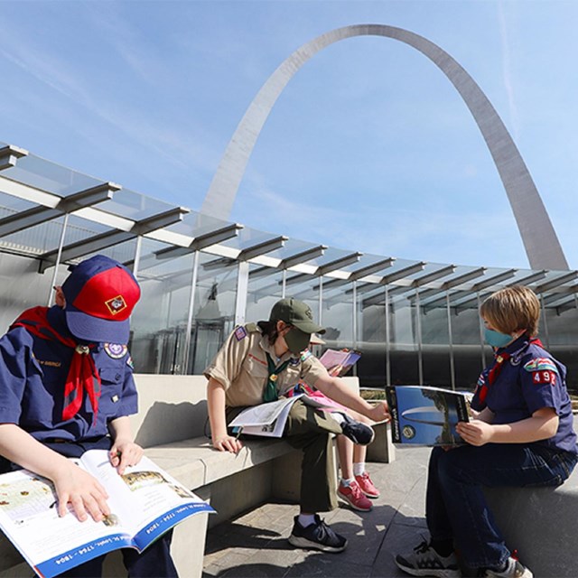 Three children sitting on a bench in front of the Gateway Arch. 