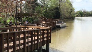 Deck with people on it next to a wide tree-lined waterway