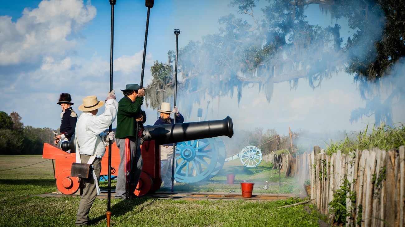 Men in period clothing stand next to a cannon with smoke filling the air.