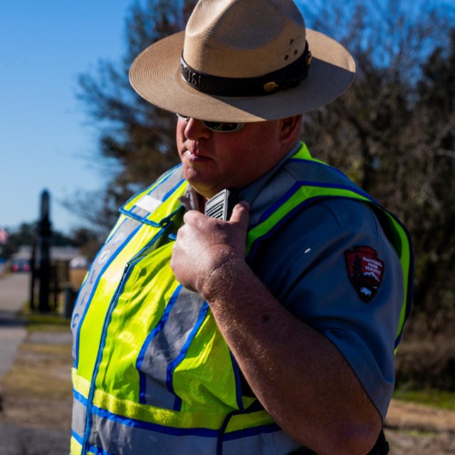 A park ranger in a safety vest talks into a radio.