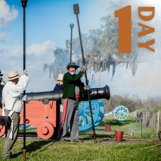 Men in period clothing stand next to a cannon, smoke fills the air. 