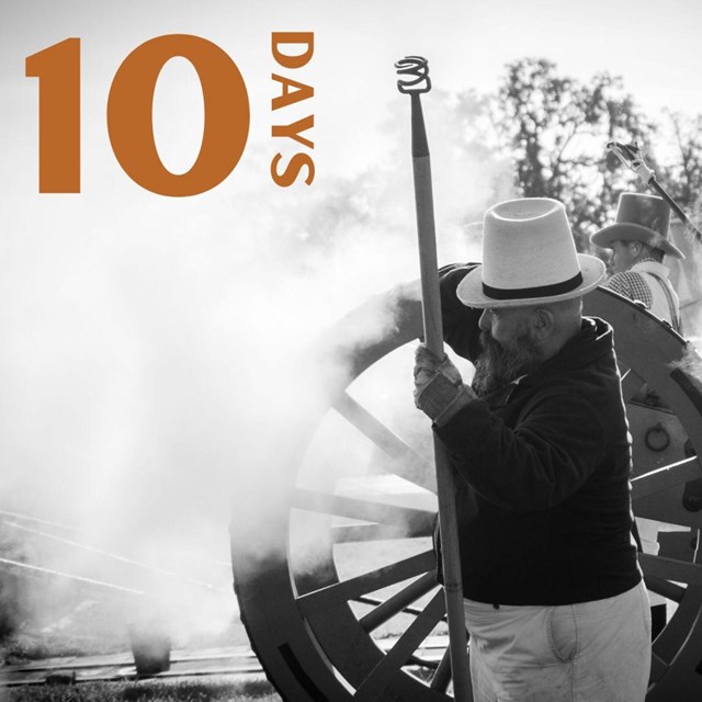 Black and white photo of a man in period clothing next to a cannon and smoke.