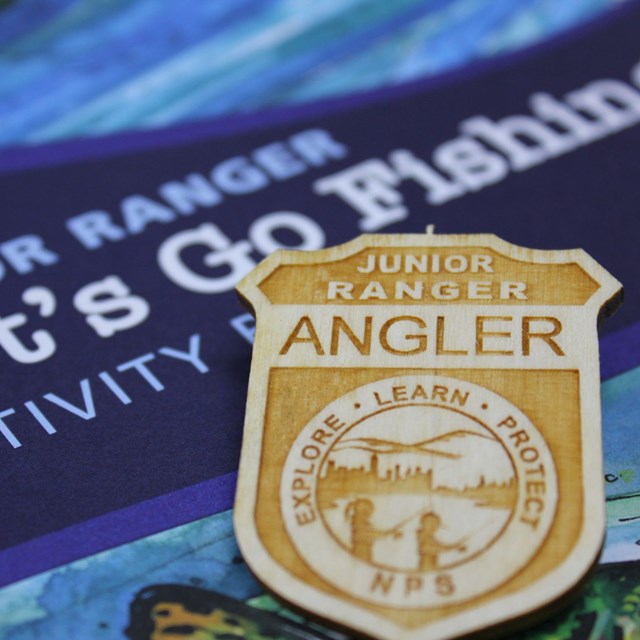 Wooden Junior Ranger Angler badge atop a blue 