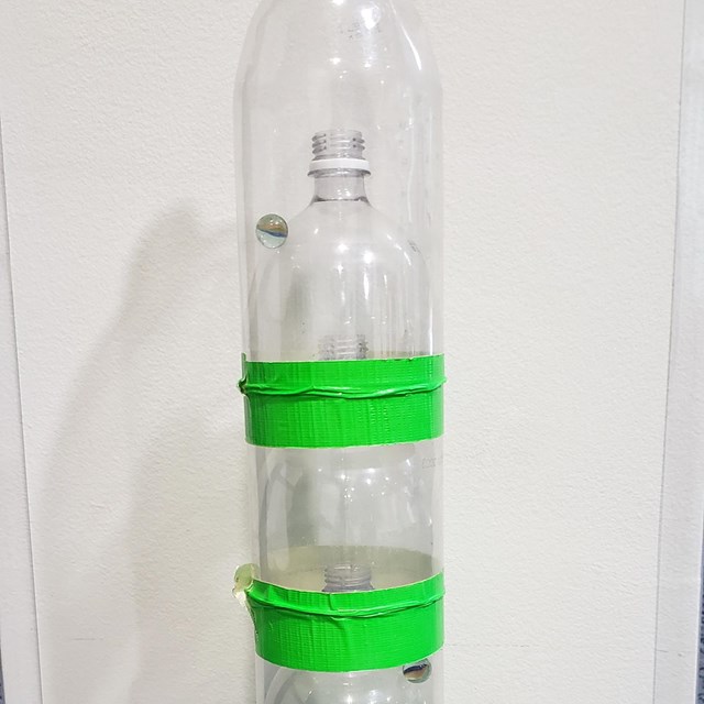 clear soda bottles nested cut open and nested within each other. taped with green tape.