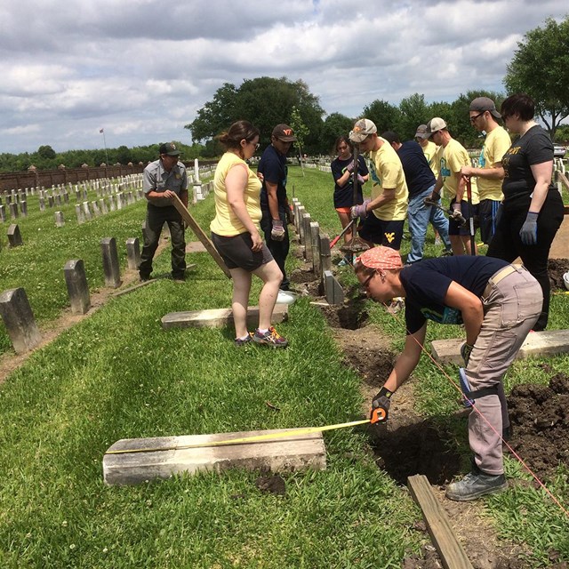 People measuring and realigning headstones