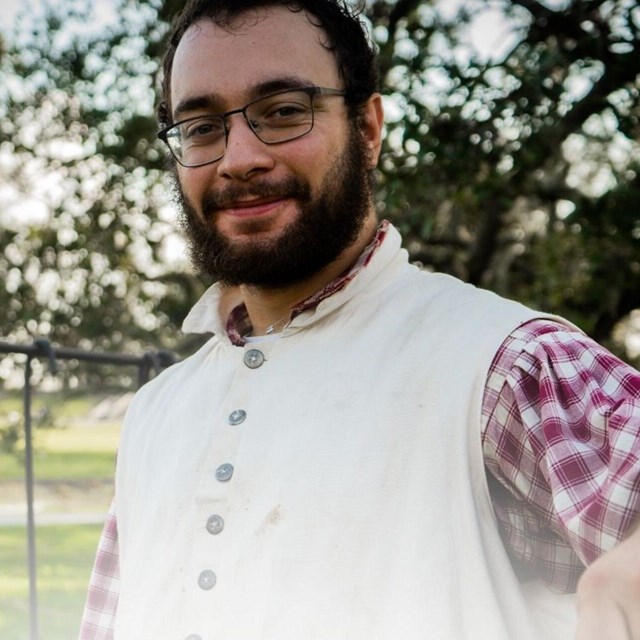 Man in period clothing holds up a serving spoon and smiles.