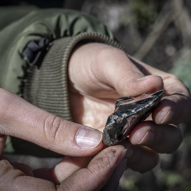 Hands hold a piece of worked obsidian.