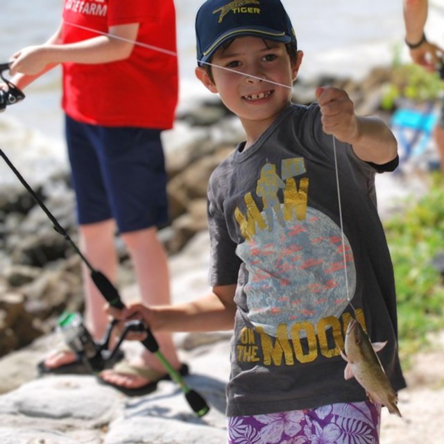 Boy stands along the shore with a fishing pole in hand.