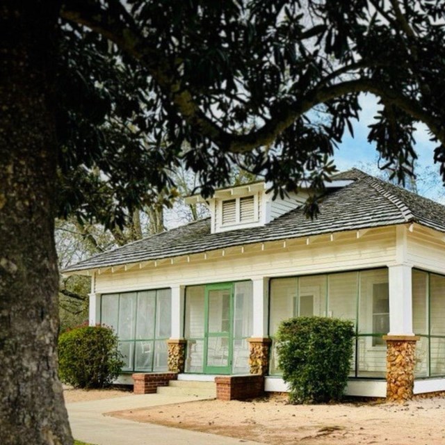 An interpretive sign stands in front of a white wooden building, on either side stand animal pens.