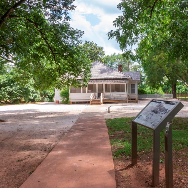 An informational sign stands in from of a historic wooden building.