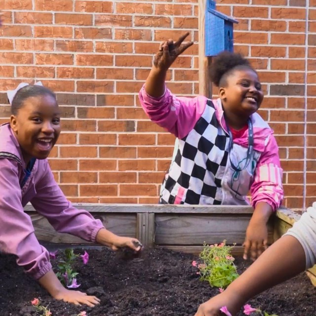 Kids digging in dirt to plant flowers. 