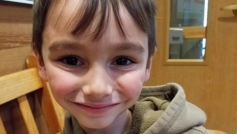 a smiling child with a junior ranger badge on his chest