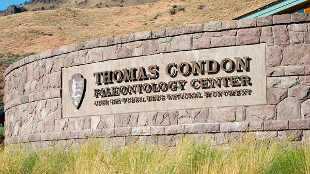 A rock wall outside of a visitor center with metal letters, "Thomas Condon Paleontology Center".