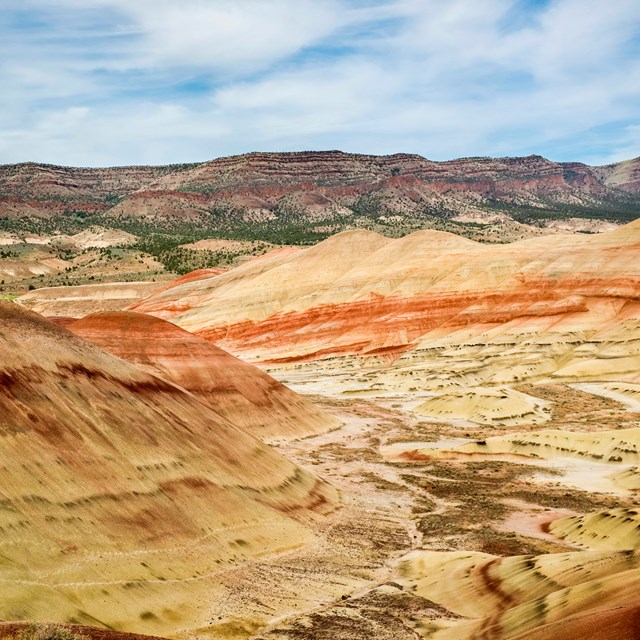 Red and yellow striped hills with a basalt ridge and cloudy blue skies in the background.