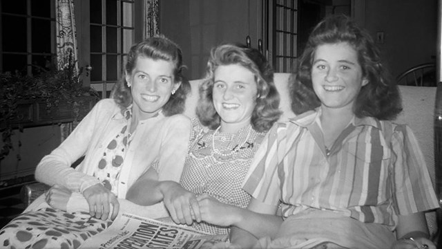 Eunice Kennedy, Kathleen Kennedy (holding a newspaper in her lap), and Jean Kennedy sit arm-in-arm.