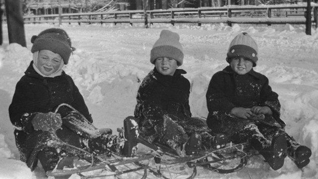 Black-and-white photo of Joe Jr., Jack, and a family friend sledding in Brookline ca. 1921-22.