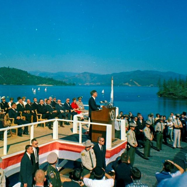 President Kennedy stands at a podium in front of a lake. 