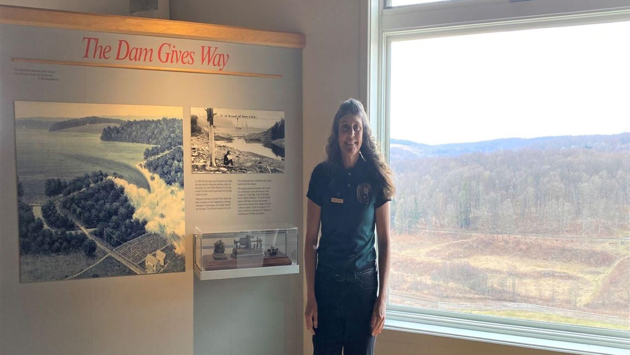 A park volunteer stands in the park visitor center next to an exhibit.
