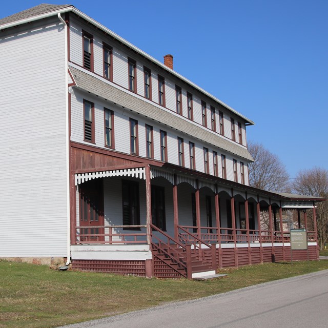 The side of a three-story building with a large porch.