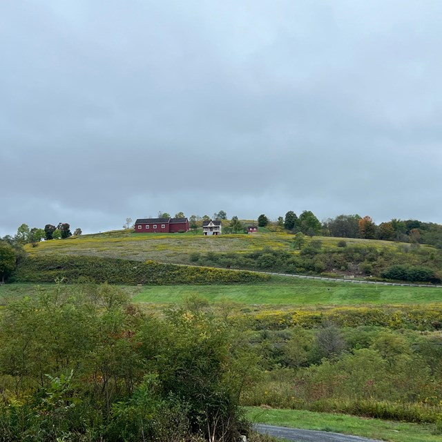 A red barn and farmhouse on a hill.
